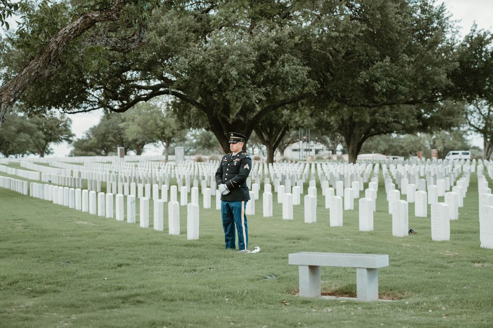A uniformed soldier stands among rows of white headstones at a military cemetery, honoring fallen heroes.