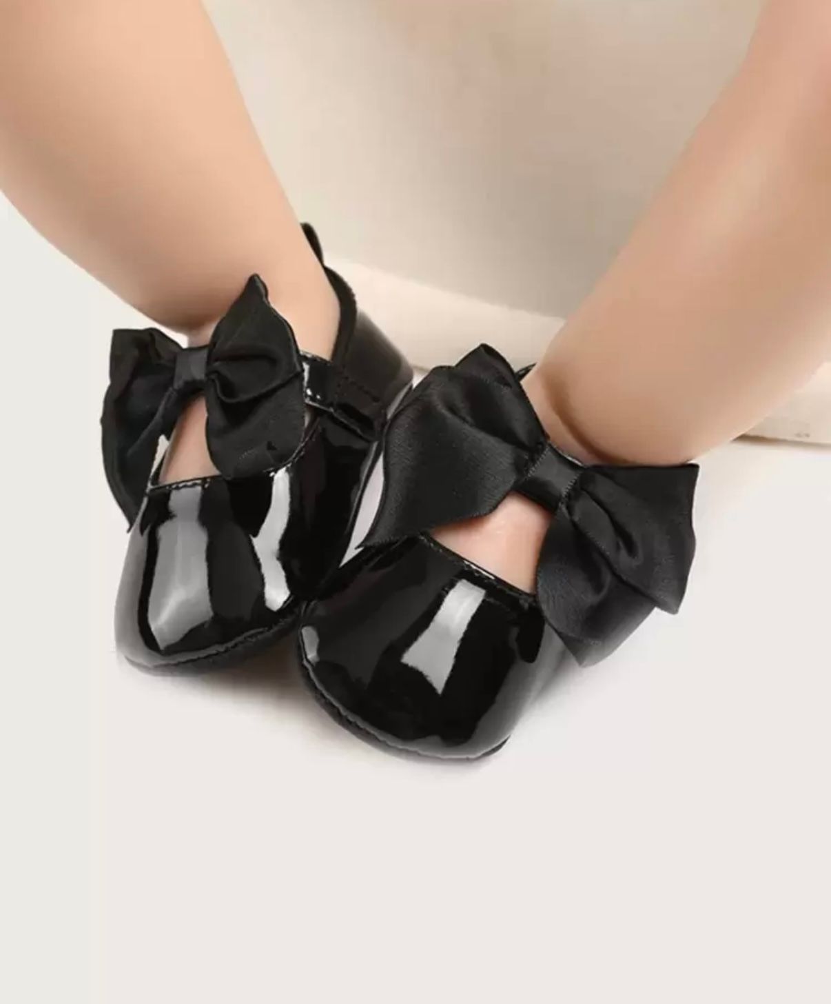 Black patent leather baby shoes with decorative bows.