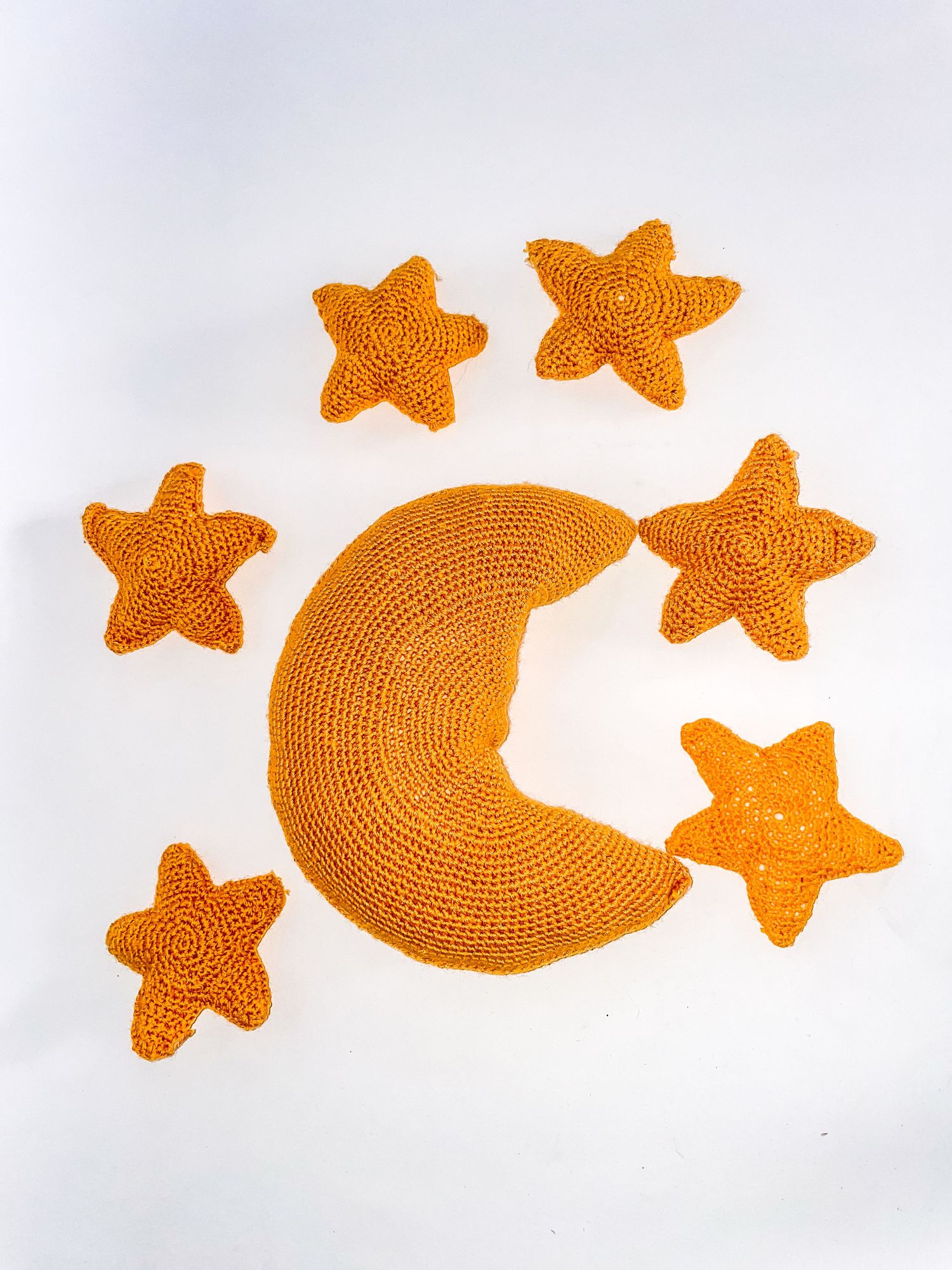 Orange crocheted moon and stars mobile elements arranged on white background.