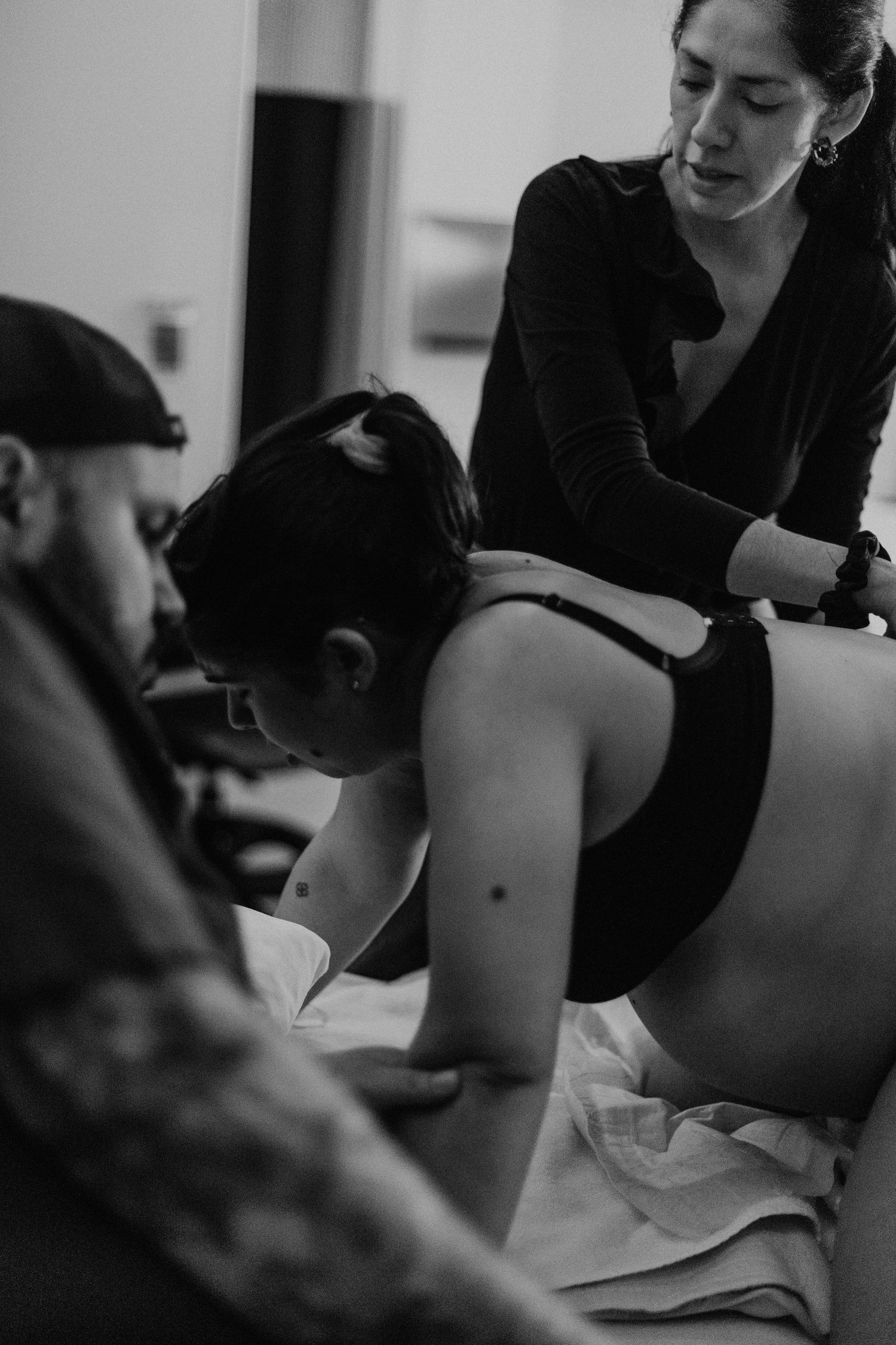 black and white photo of apregnant woman on the birth centre wearing a black bro, with her husband and doula helping her during contractions