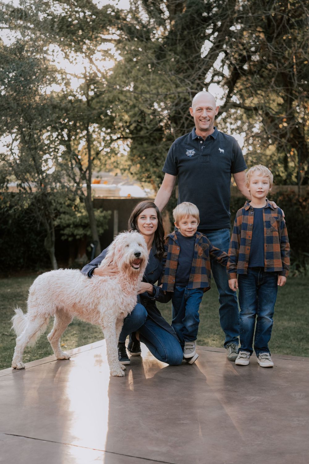 Group poses with fluffy white dog on concrete patio during outdoor family photoshoot.