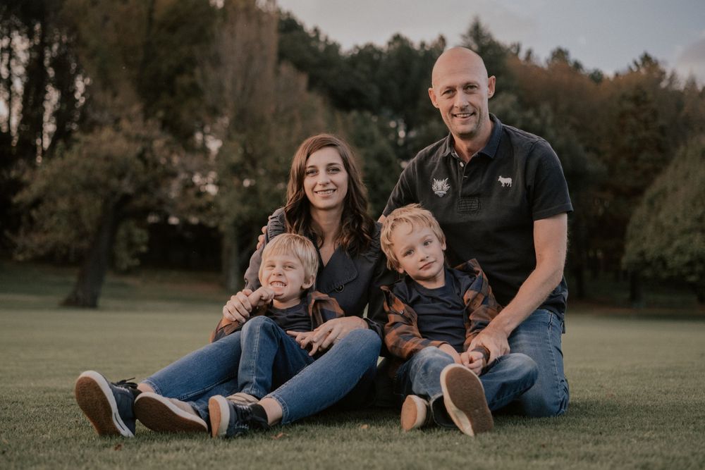 Family of four sits casually together on grass during outdoor portrait session.