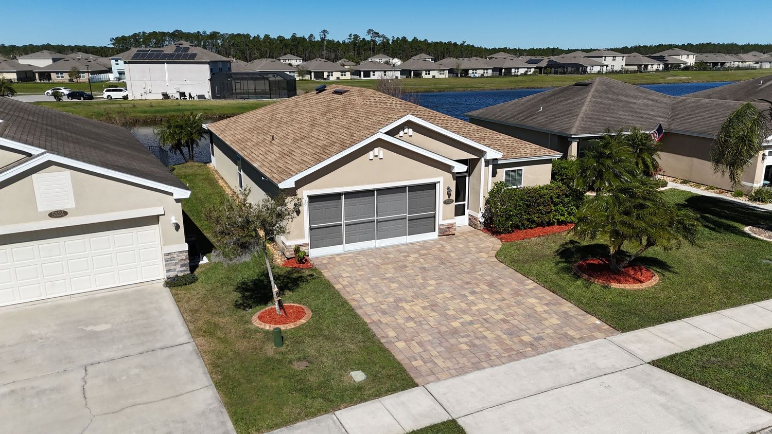 Single-story beige home with paver driveway and landscaped yard in a suburban development.