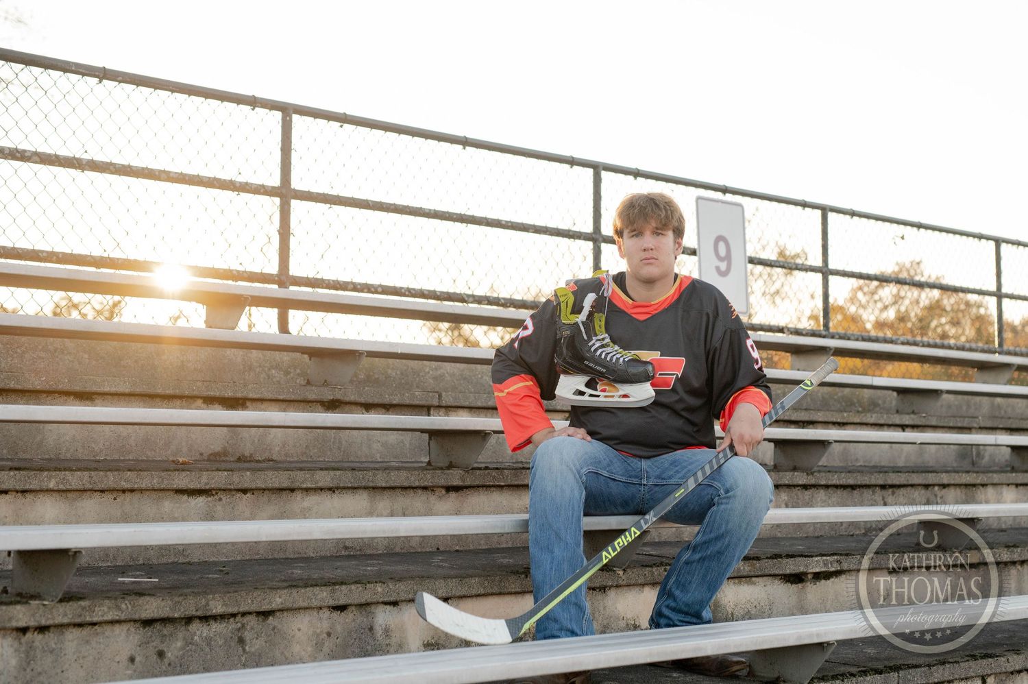 Player rests on stadium bleachers at golden hour with hockey equipment.