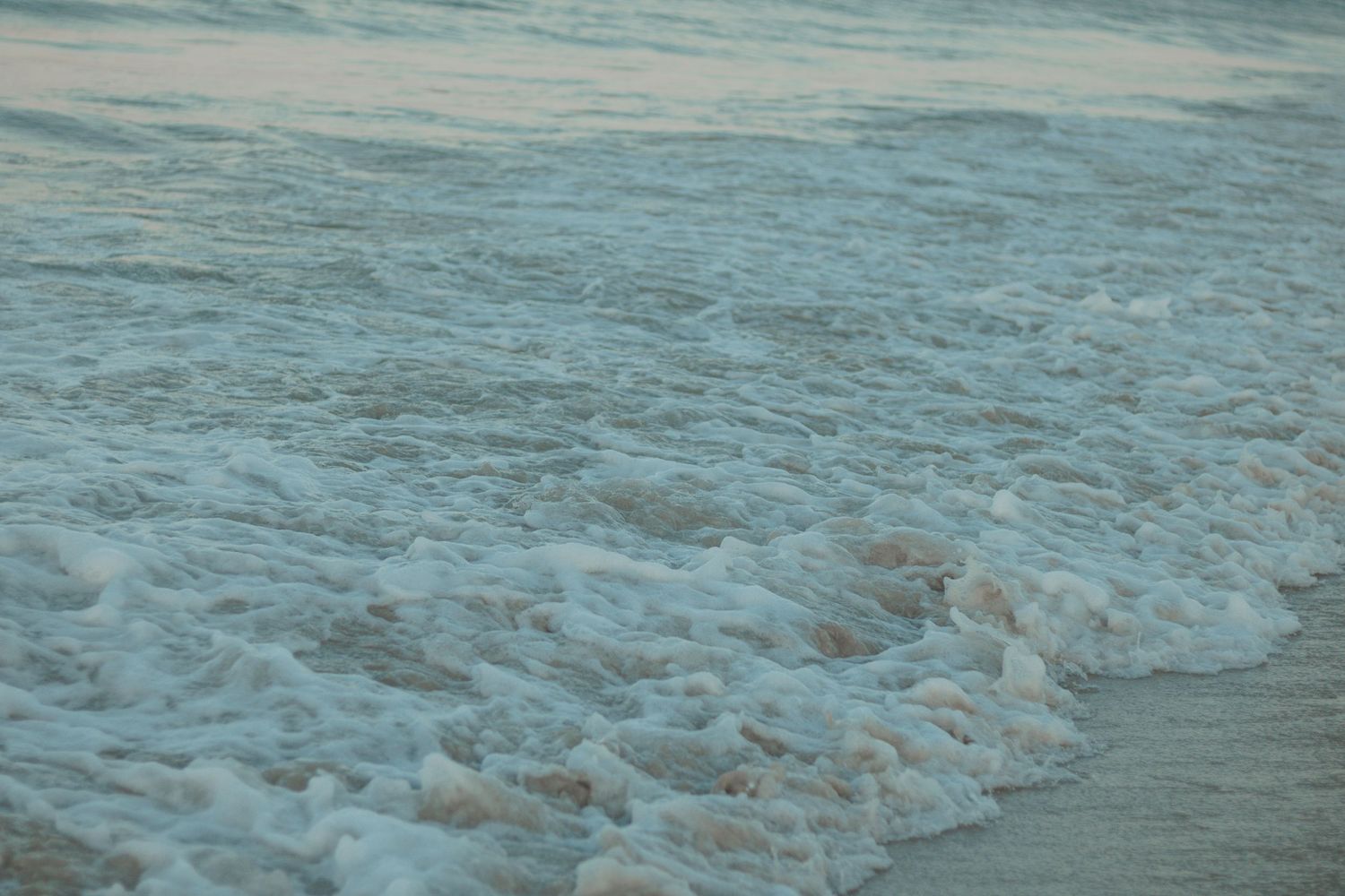 Gentle waves washing up on sandy beach with soft foam patterns.