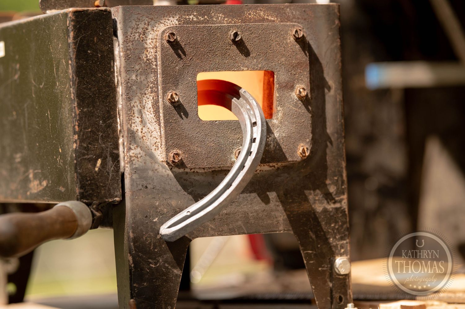 Glowing hot horseshoe visible through metalworking equipment opening.