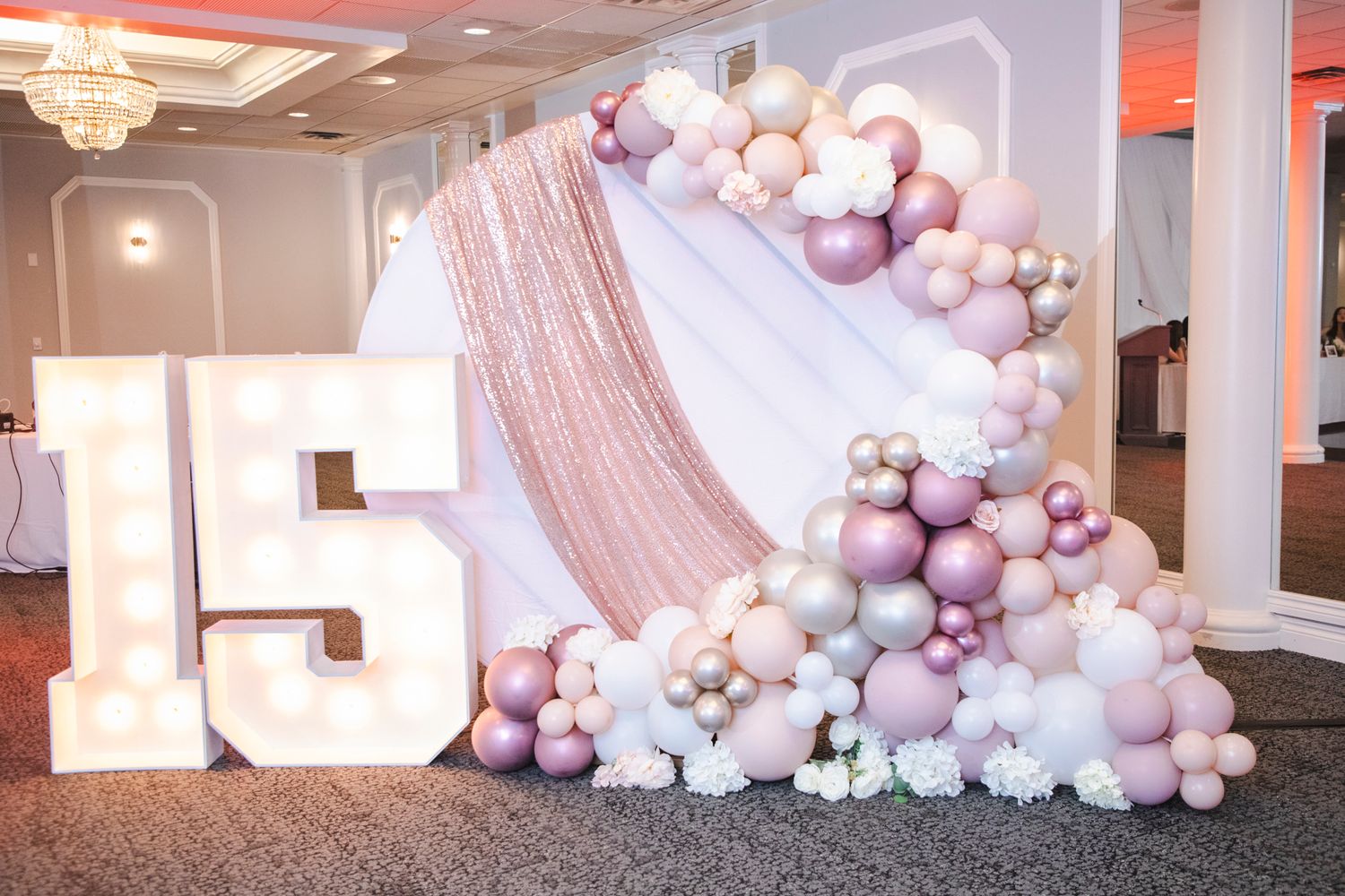 Large number 15 display decorated with pink and white balloon garland for celebration event.