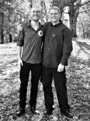 Wedding party members in black attire pose for casual photos on fallen autumn leaves.