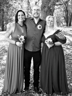 Wedding party members in dark dresses and formal wear pose together against a natural forest backdrop.