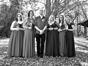 Full wedding party portrait with bridesmaids in matching dresses standing in a forest setting.