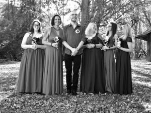 Formal wedding party lineup with bridesmaids in matching dresses against a wooded background.