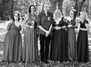 Wedding group photo featuring bridesmaids in matching dresses surrounded by autumn foliage.