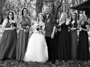 Large wedding party poses together outdoors with bridesmaids in matching dresses and white bridal gown.