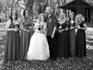 Complete wedding party portrait with bride in white and attendants in dark dresses in forest setting.