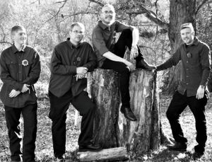 Wedding party members in dark suits pose casually outdoors in a black and white photo.