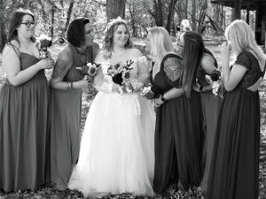 Bridesmaids in gray dresses stand with bride in white gown during outdoor forest photoshoot.