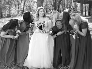 Wedding party members pose together in gray dresses and white gown against natural woodland backdrop.