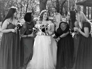 Wedding group photo showing bridesmaids in matching gray dresses with bride in white gown outdoors.