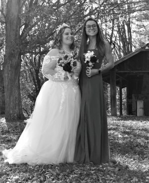 Black and white wedding photo of bridal party members posing casually in a wooded setting.