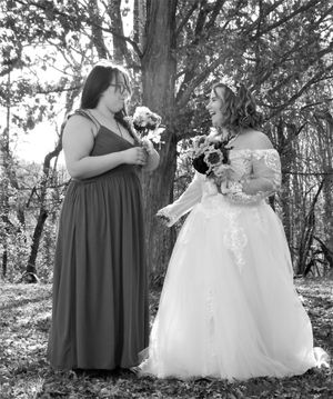 Wedding party members in gray and white dresses pose against trees in natural lighting.