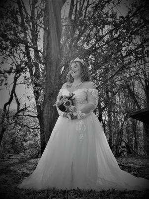 Artistic black and white photo captures someone in an elegant white dress in a serene forest setting.