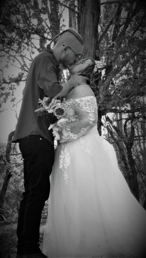 A romantic black and white wedding photo series showing a couple embracing outdoors among trees.