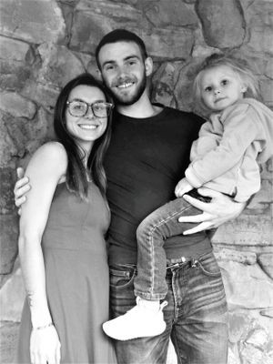 A family of three poses together against a stone wall background in black and white.