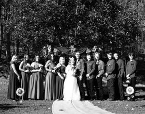 Wedding party members line up outdoors with bridesmaids in matching gowns and groomsmen in dark attire.