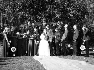 A group of wedding attendees stand together in a line outdoors on a sunny day.