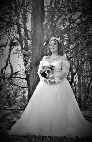 Black and white photo of a bride in a ballgown dress posing in nature.