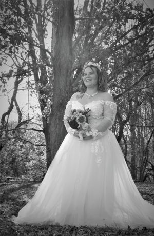 A bride in a flowing white ballgown poses in a wooded outdoor setting.
