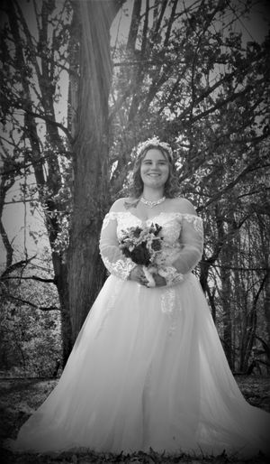 Black and white portrait of a bride in a flowing white ballgown dress standing among trees in a forest setting.