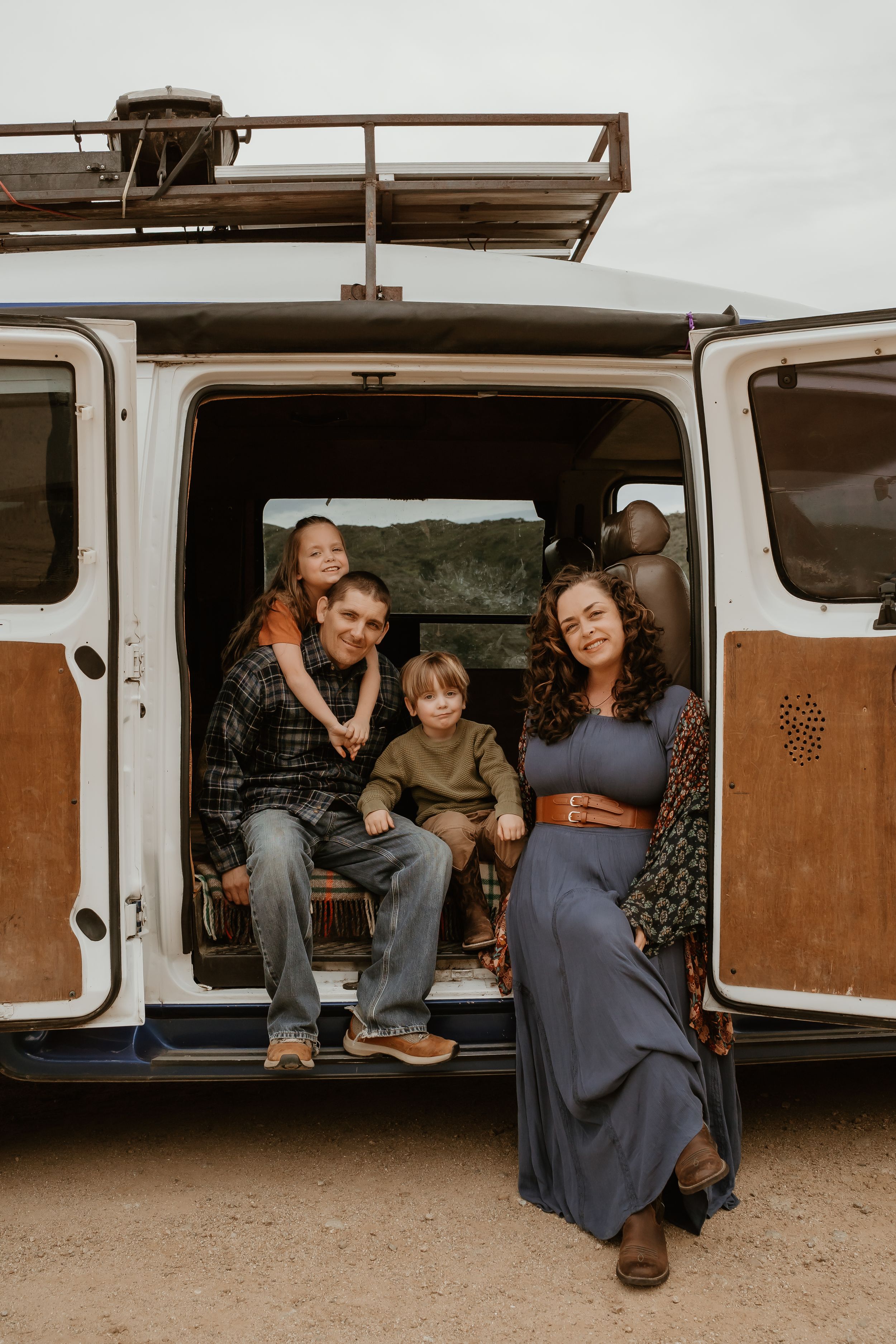 Family sitting together in open door of vintage van with mountains in background during autumn road trip.