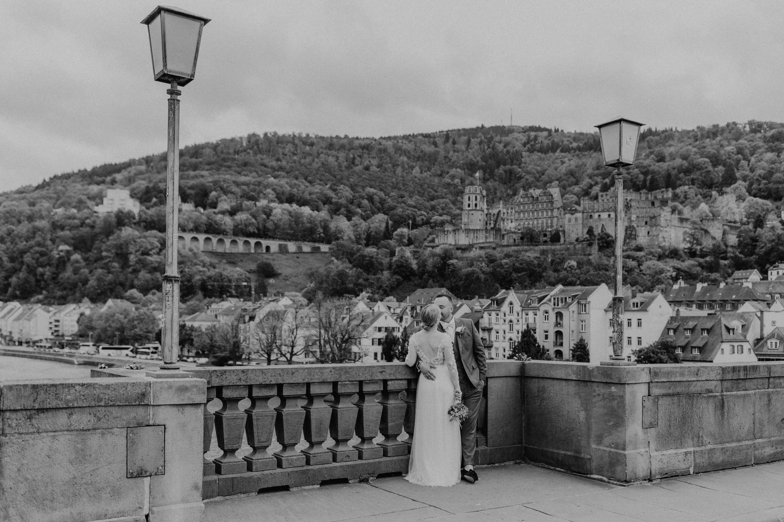 Brautpaar, das auf der alten Brücke in Heidelberg steht und sich küsst. Man sieht die Heidelberger Kulisse mit Schloss im Hintergrund.