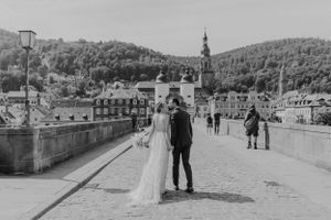 Schwarzweiß-Bild eines Brautpaars, das über die alte Brücke in Heidelberg läuft und sich küsst. Im Hintergrund sieht man den Brückenkopf.