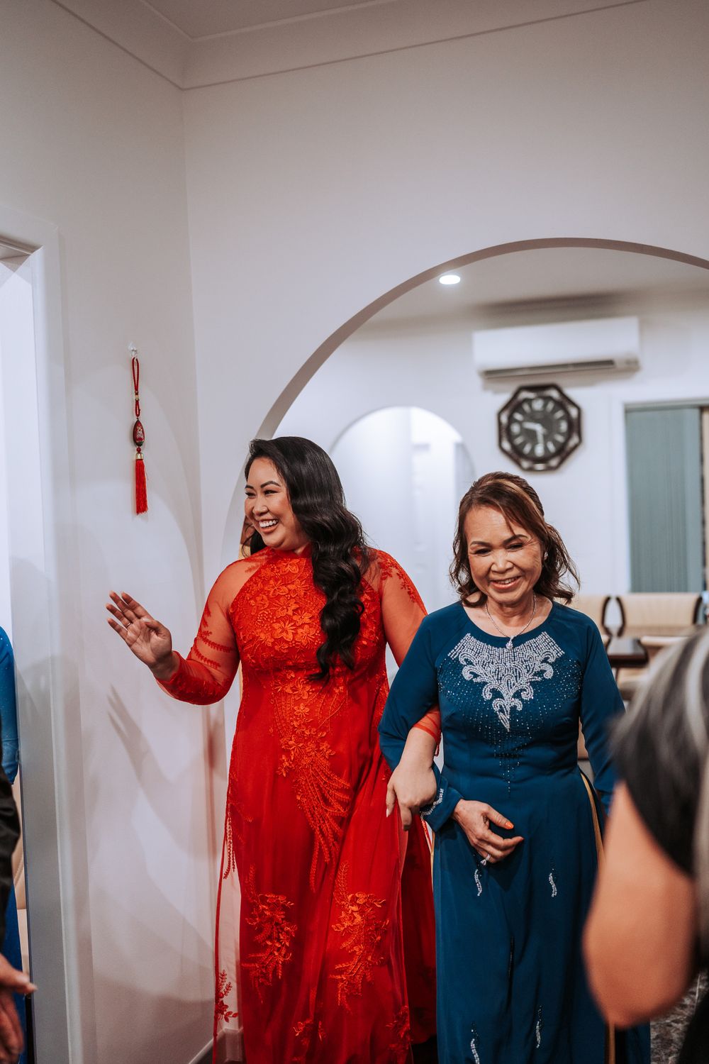 Two women in formal red and blue dresses celebrate in an interior hallway.