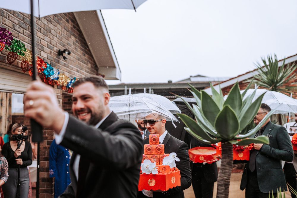 A festive outdoor wedding celebration with umbrellas and decorative flowering plants at a brick venue.