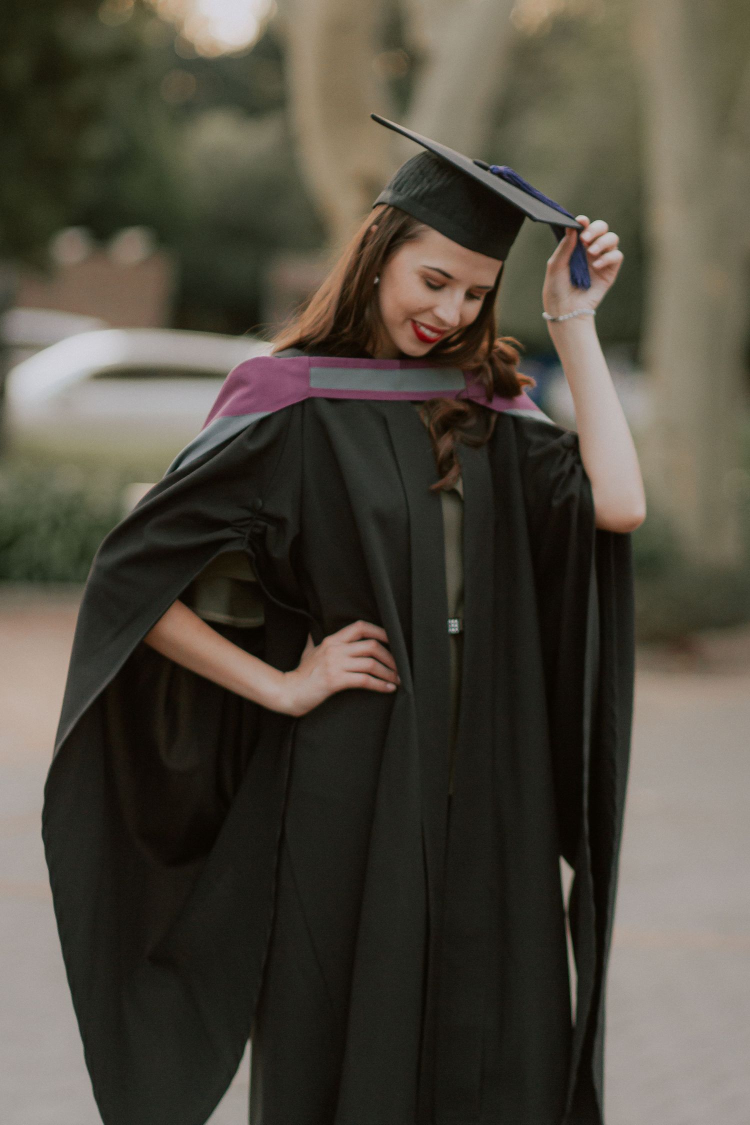 A graduate in traditional cap and gown posing playfully outdoors.