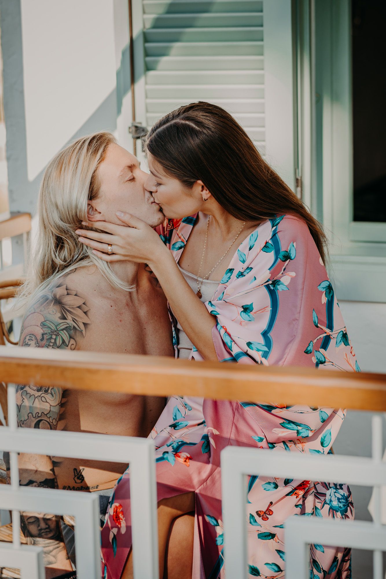 A tender romantic moment shared between two people in summer attire on a sunlit porch.