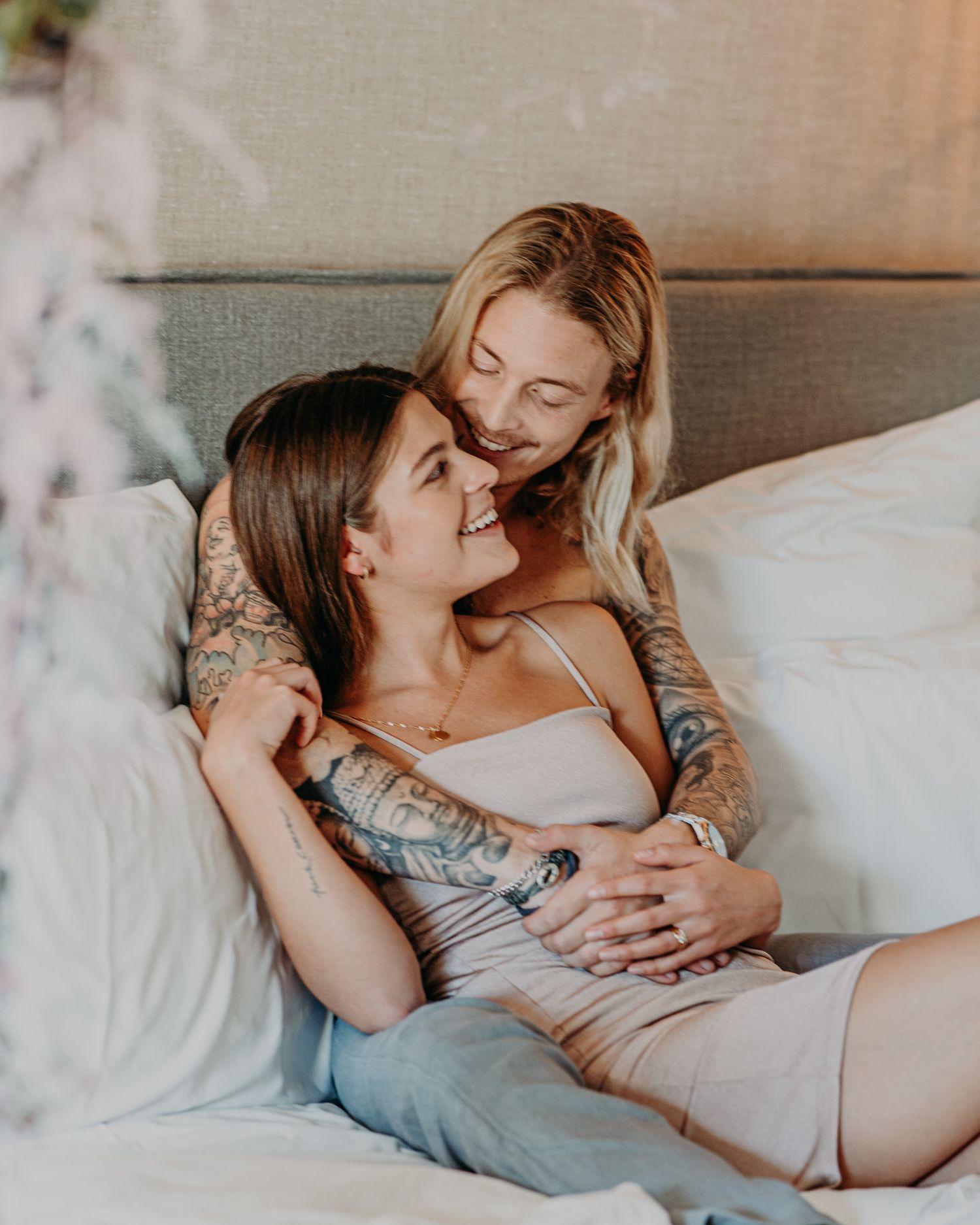 A couple embraces intimately on a bed, sharing a tender moment in soft lighting.