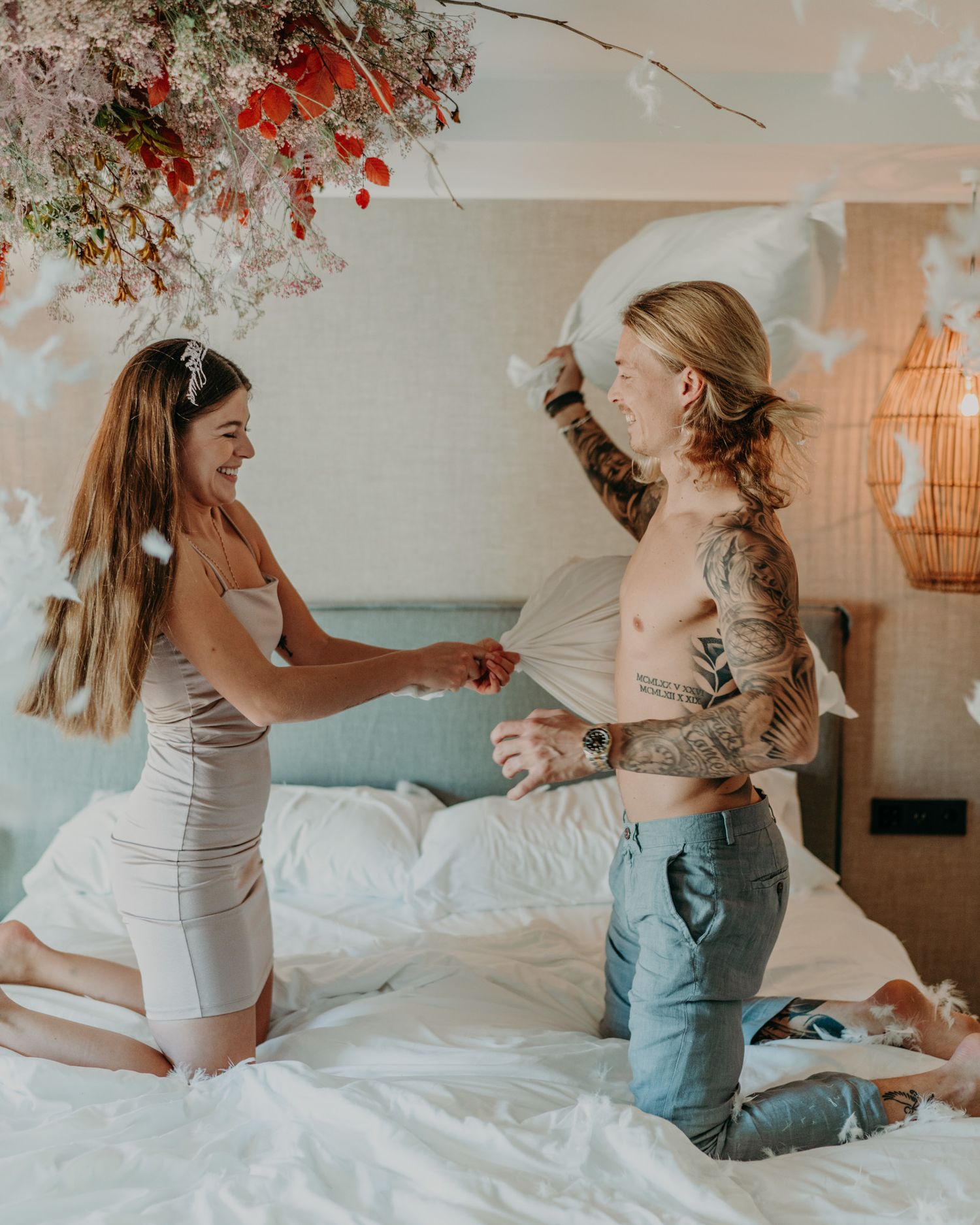 Two people laughing and having fun together during a playful moment on a bed with autumn decorations visible.