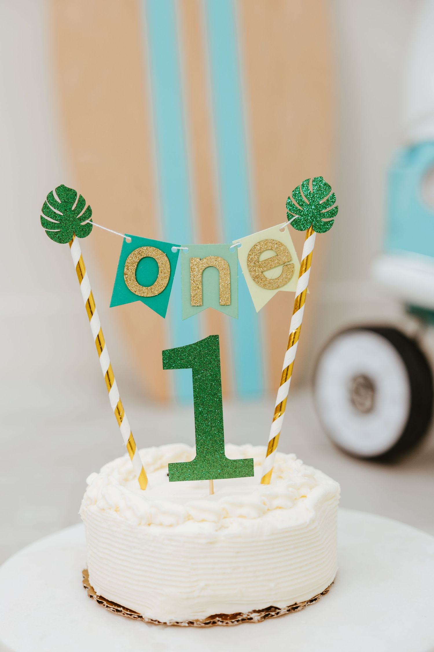 White birthday cake with tropical leaf banner and number one topper.