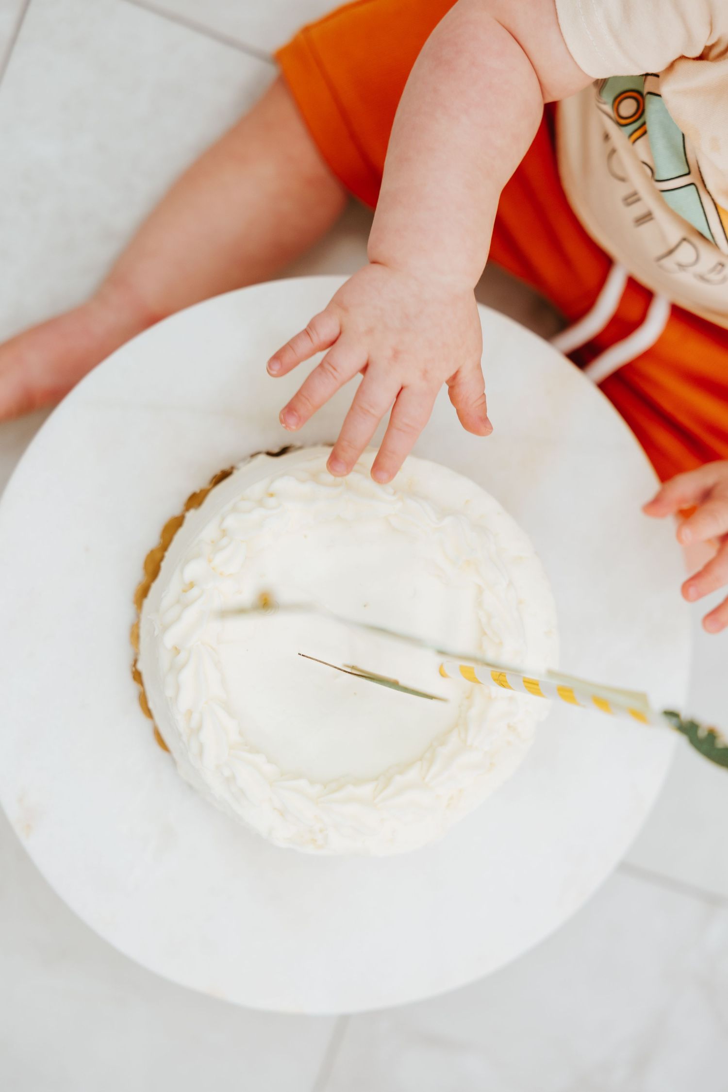 Small hands reaching towards a white frosted birthday cake on a plate.