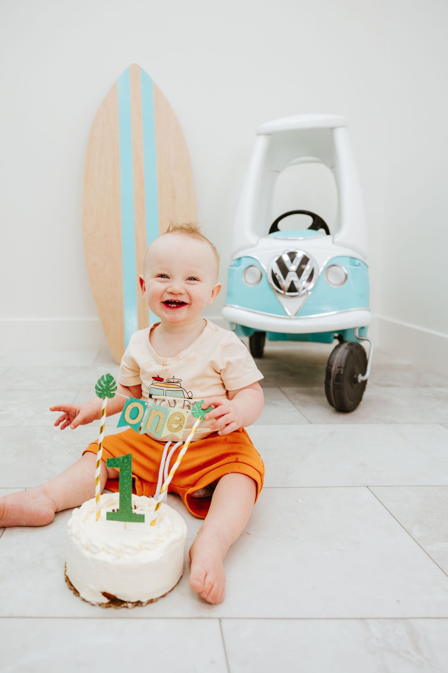 First birthday setup with cake, decorative surfboard, and light blue VW toy car.