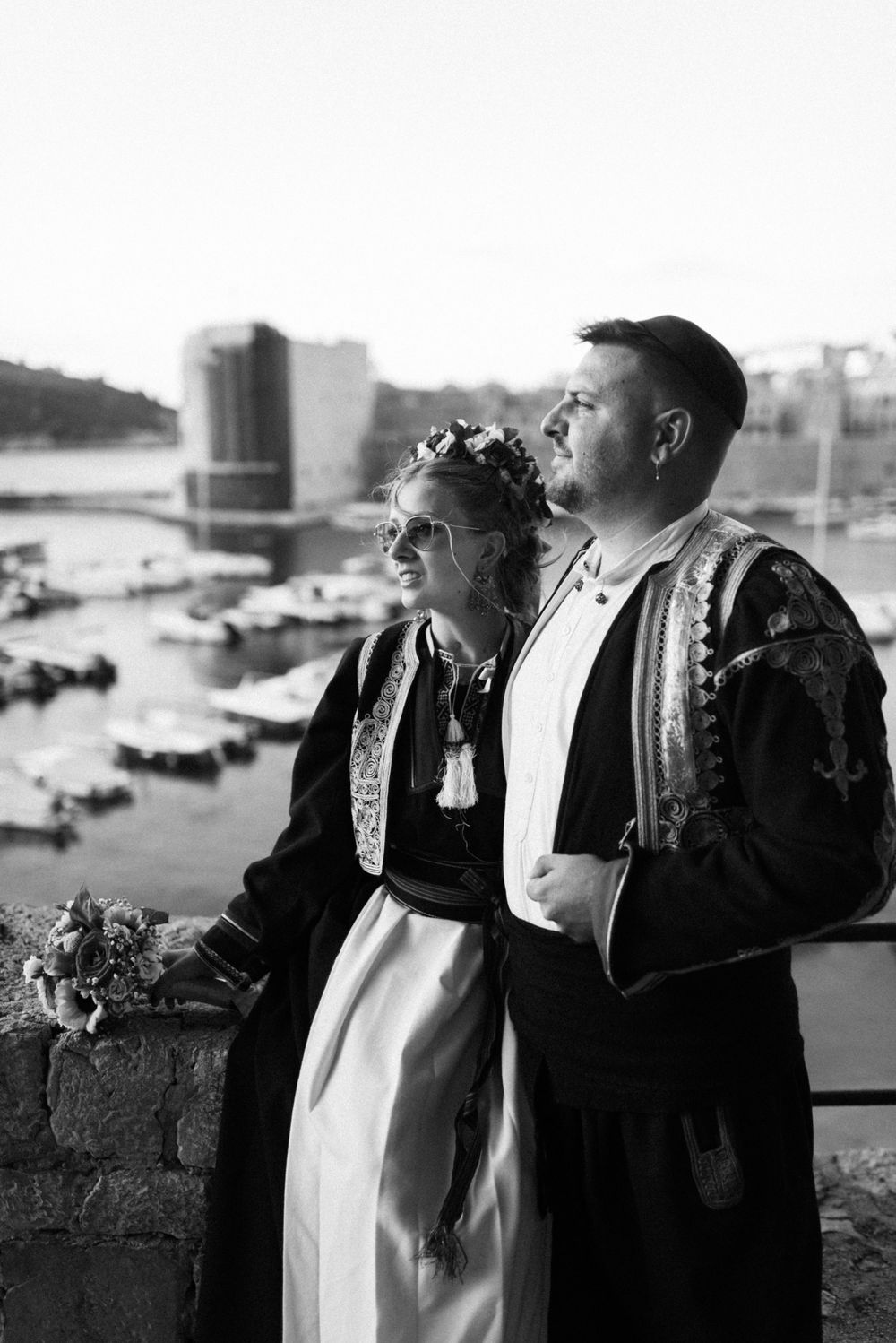 A couple in traditional wedding attire poses together against a cityscape backdrop.