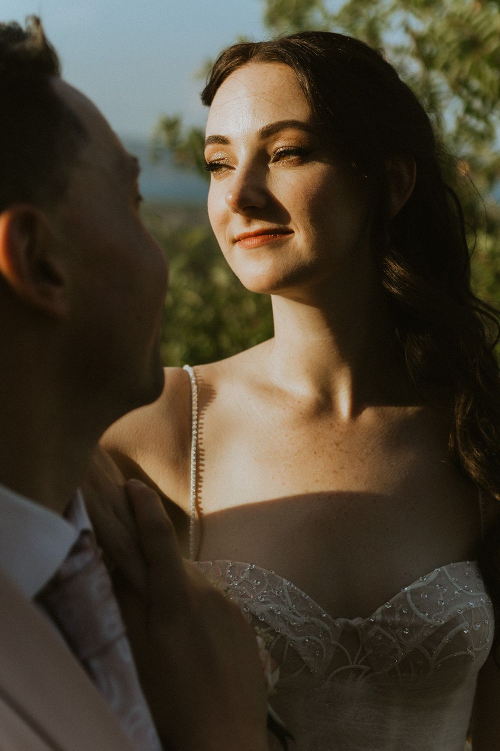 A romantic golden hour portrait of a bride in a lace wedding dress gazing lovingly at their partner.