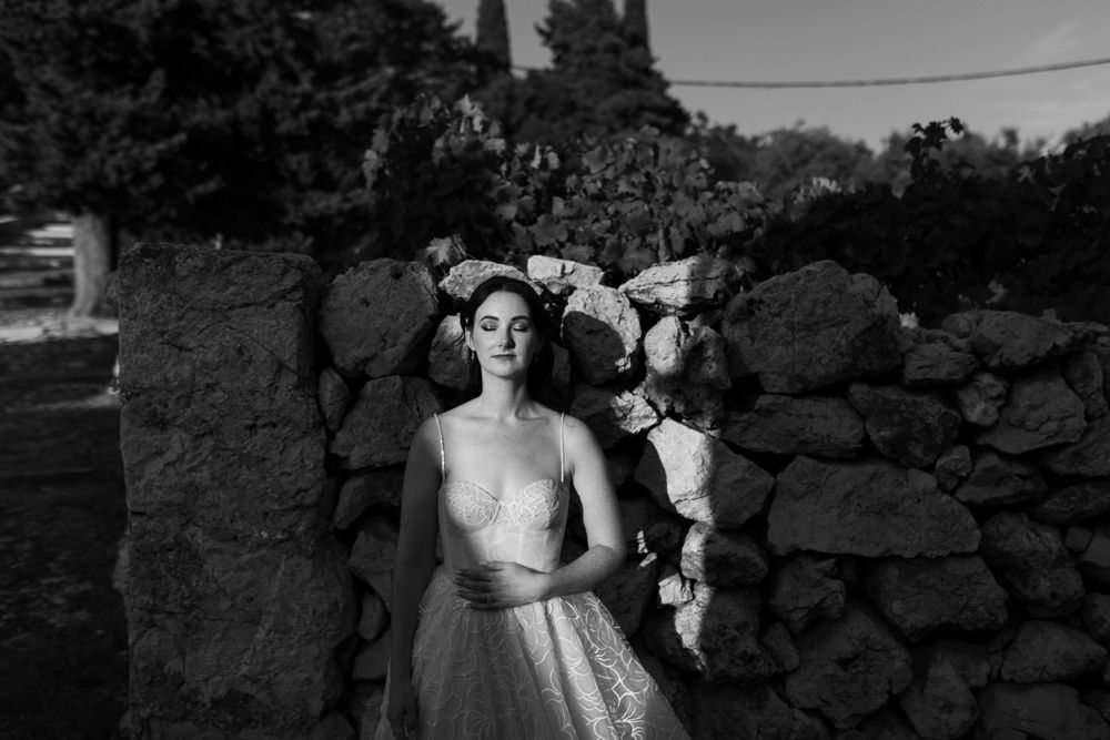 A black and white portrait of a bride standing against a rustic stone wall.