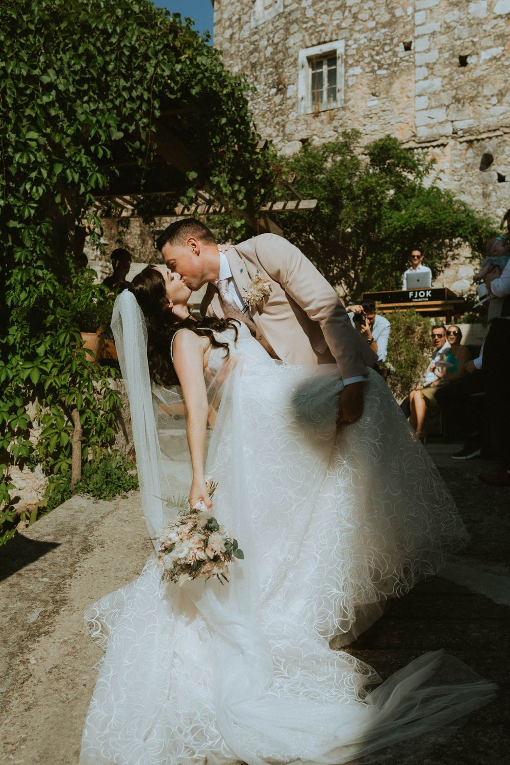 A romantic wedding couple shares a kiss in front of an ivy-covered stone wall.