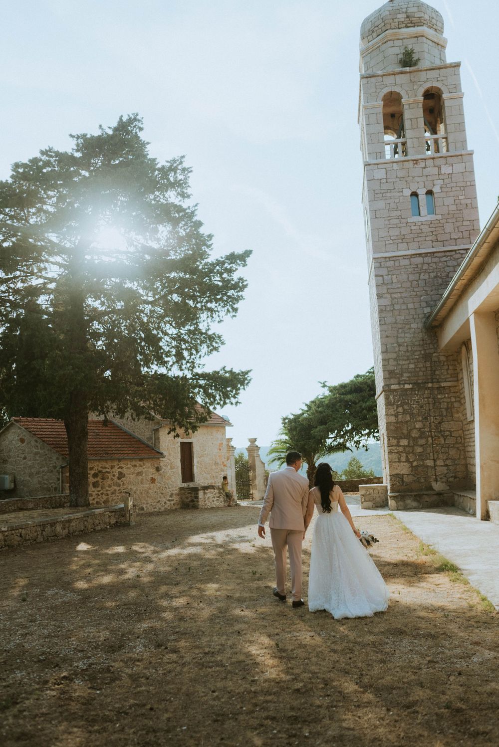 A couple walking toward a stone bell tower outside a historic church.