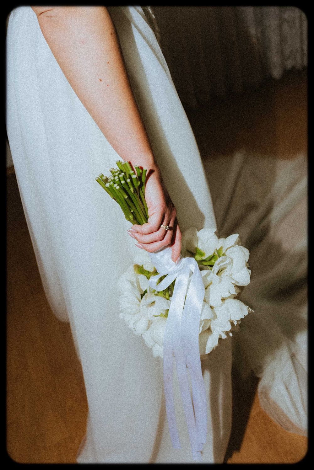 Close-up of a white wedding dress detail with white lily bouquet and ribbon.